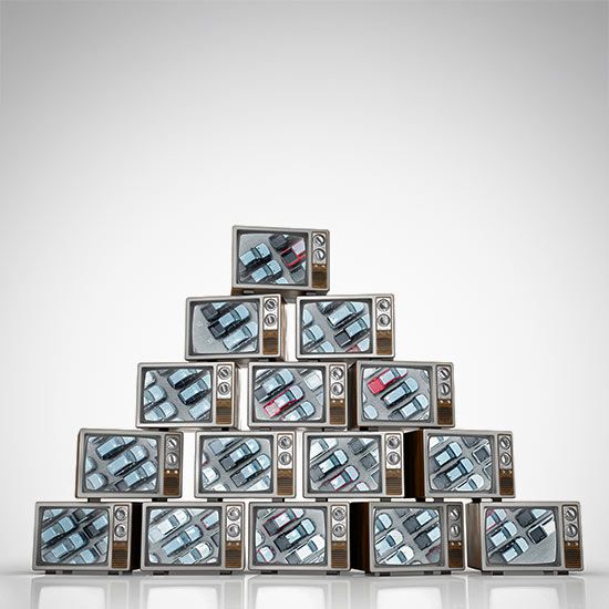 Pyramid of old CRT TV's showing an image of a dealership parking lot on the screen.